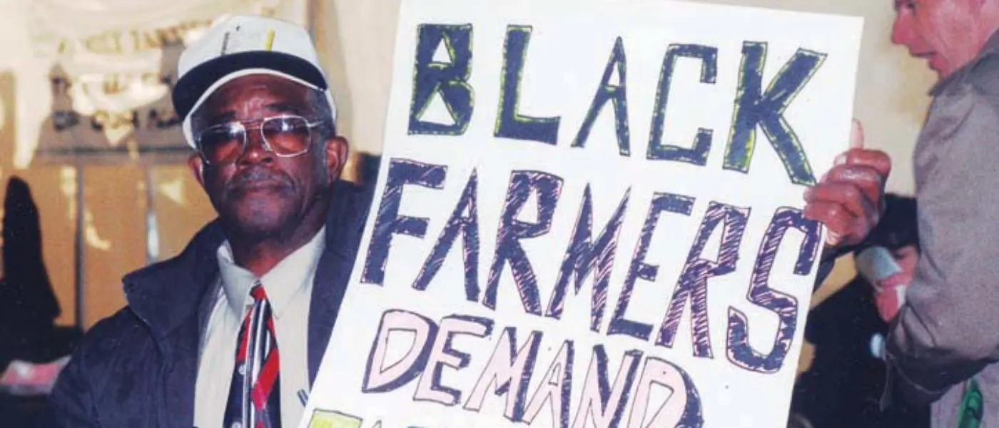 Black farmer holds signs that reads Black farmers demand fair prices