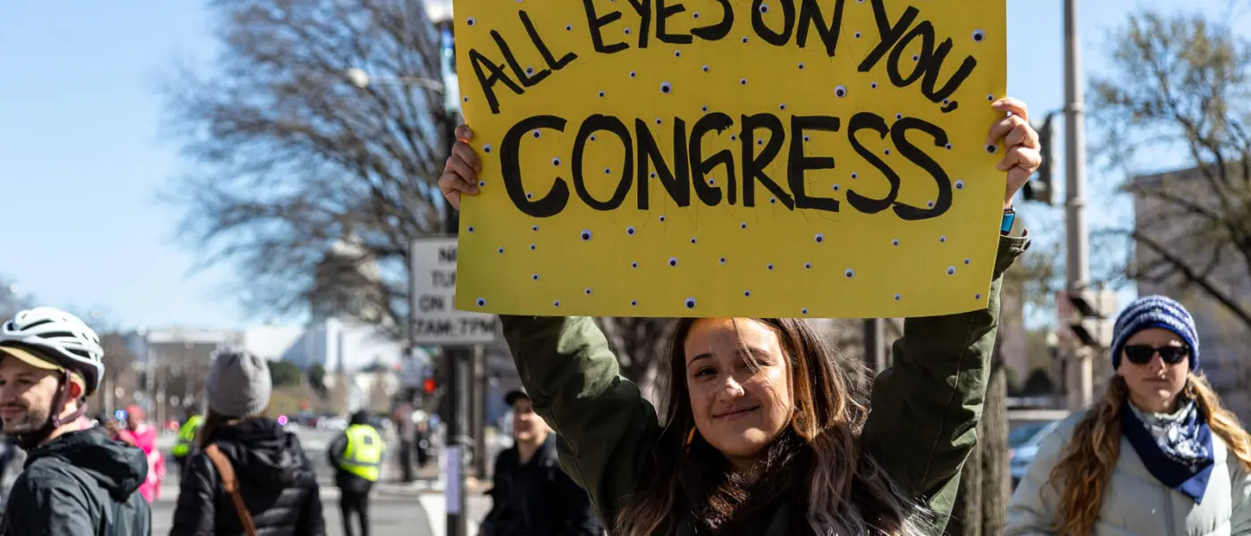Activist with "All Eyes On You, Congress" sign