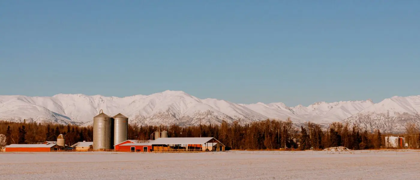 snowy farm scene in front of snowy mountains