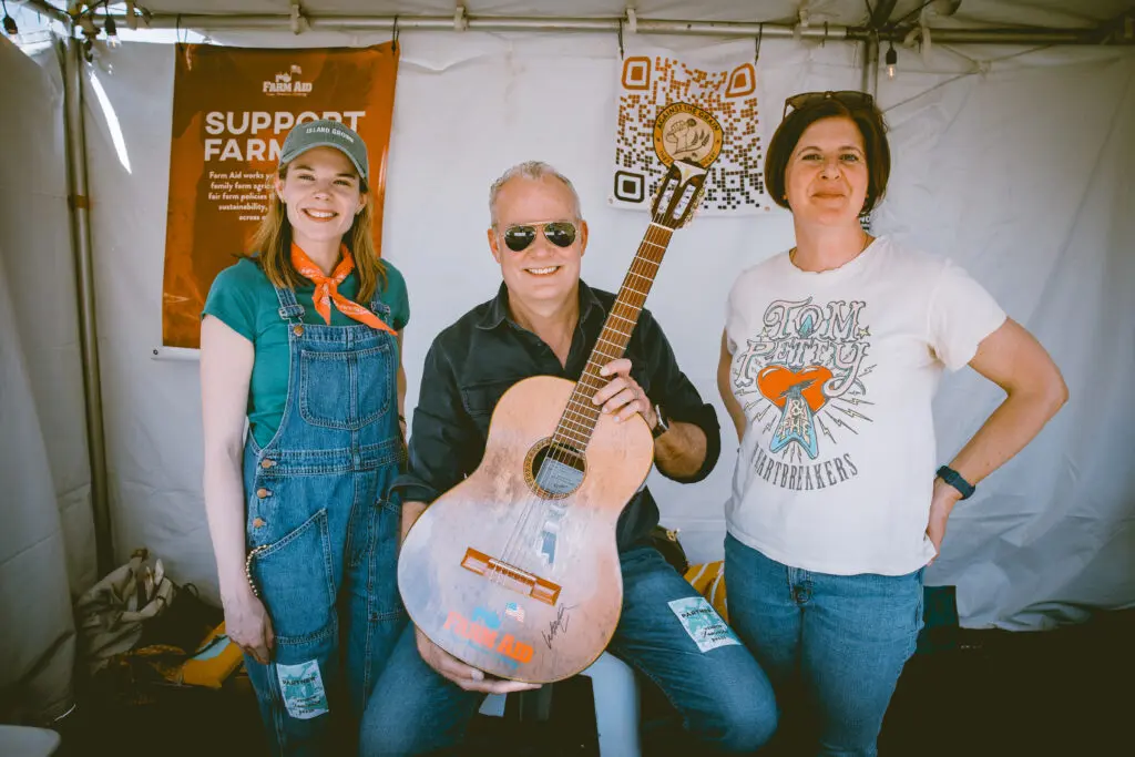 Farm Aid staff people posing while holding a guitar
