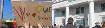 child holding a sign at a rally that says "We [heart symbol] our farmers"