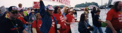 Neil Young marching holding a sign that says REGULATE HOG FACTORIES on it
