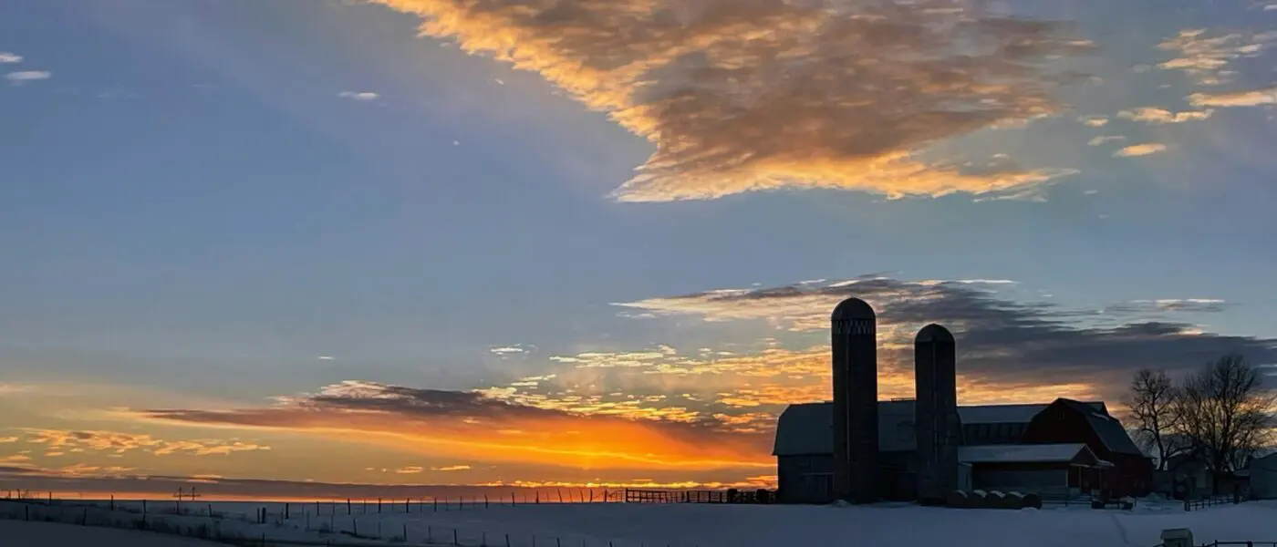Sunset over a snowy farm with silos.