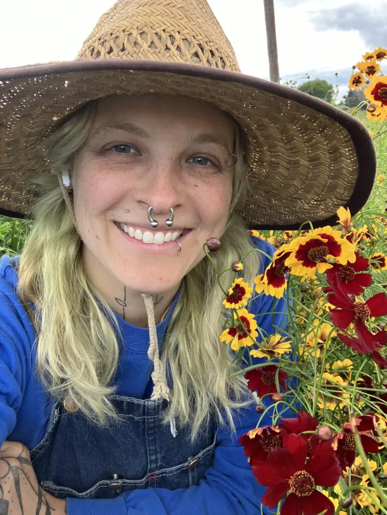 Person wearing a hat and smiling in front of flowers