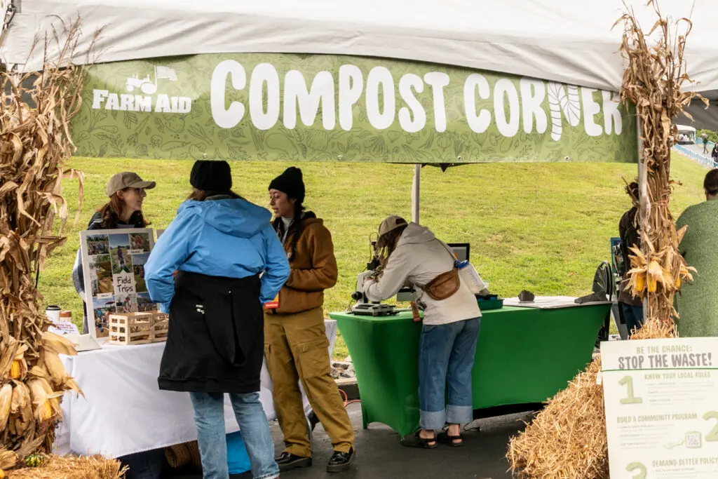 People engaging with a "compost corner" booth at Farm Aid 2026