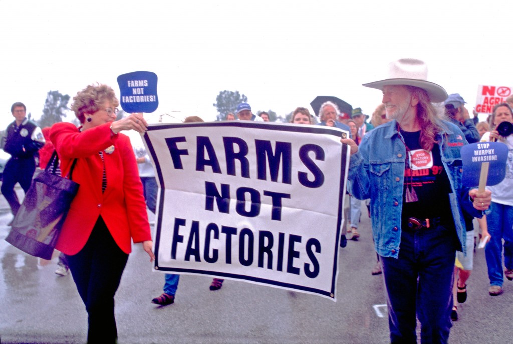 Willie Nelson marching in a protest holding a sign that says, "Farms Not Factories"