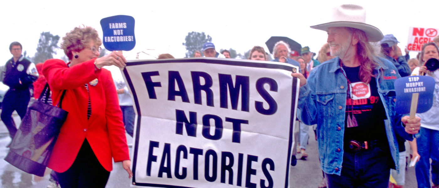 Willie Nelson marching in a protest holding a sign that says, "Farms Not Factories"