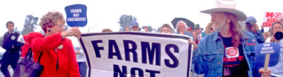 Willie Nelson marching in a protest holding a sign that says, "Farms Not Factories"