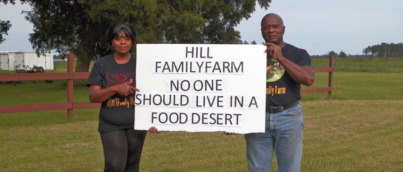 Eunice and Sylvester Hill holding a sign that says "Hill Family Farm No One Should Live In A Food Desert"