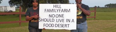 Eunice and Sylvester Hill holding a sign that says "Hill Family Farm No One Should Live In A Food Desert"