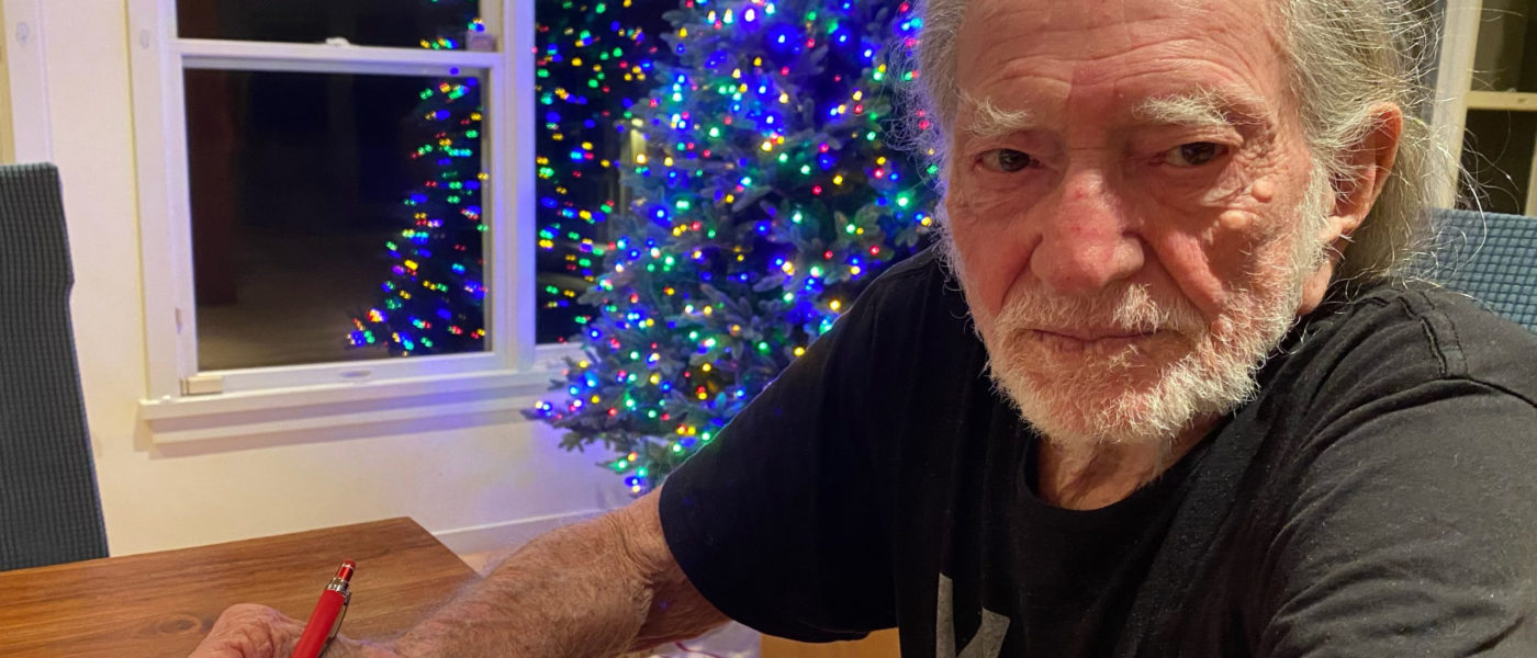 Willie Nelson signing Farm Aid grant checks in front of a Christmas tree