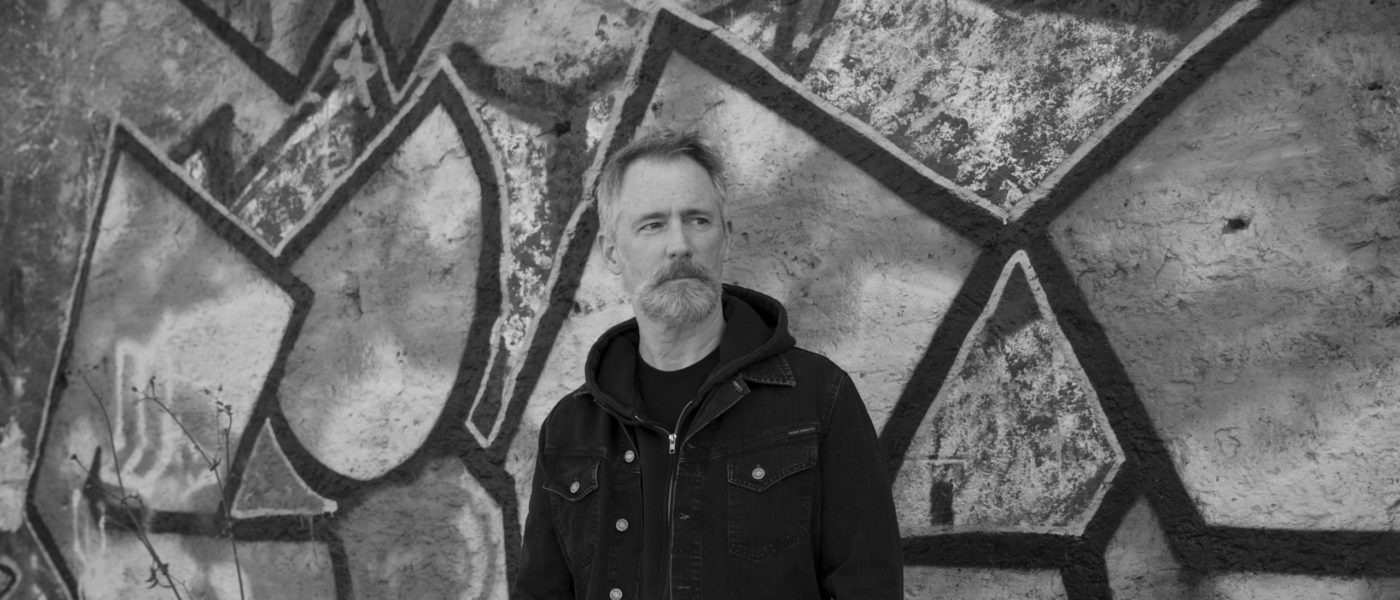 Michael Stewart Foley in front of a grafitti covered wall