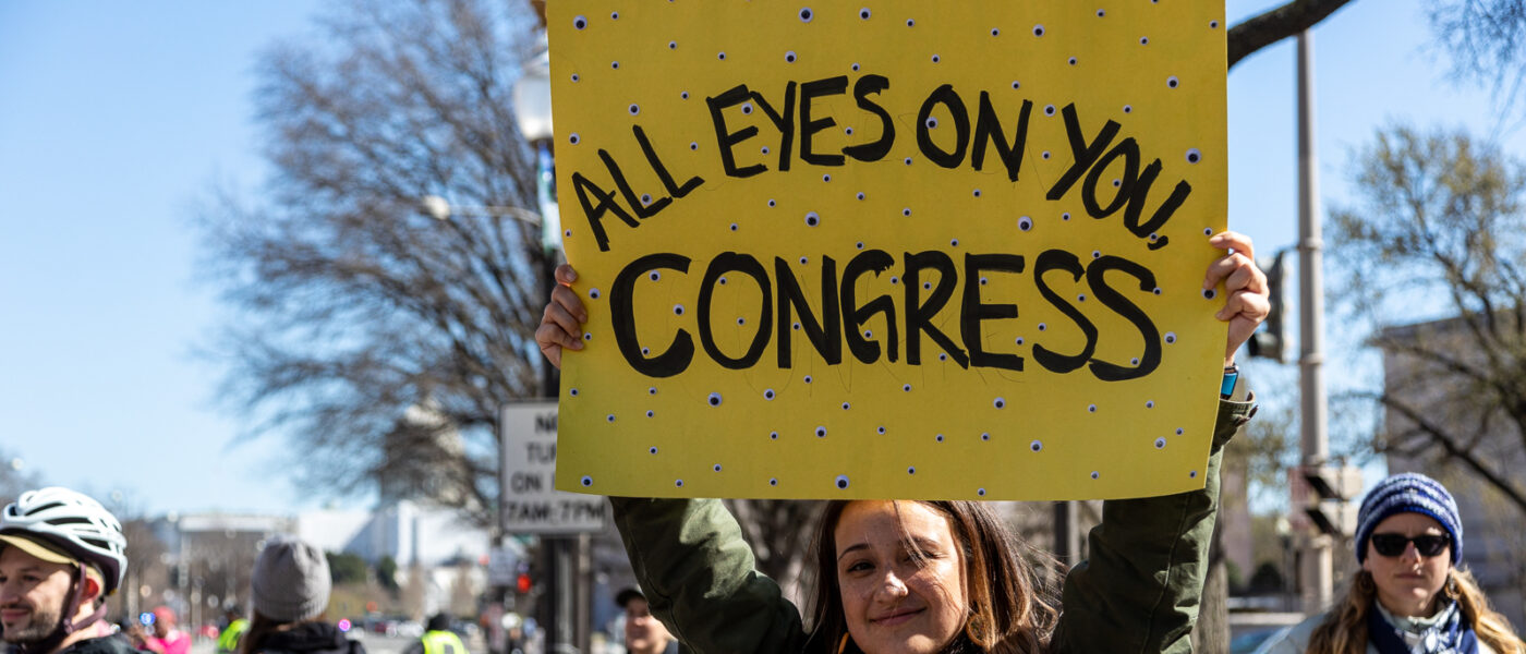 Activist with "All Eyes On You, Congress" sign