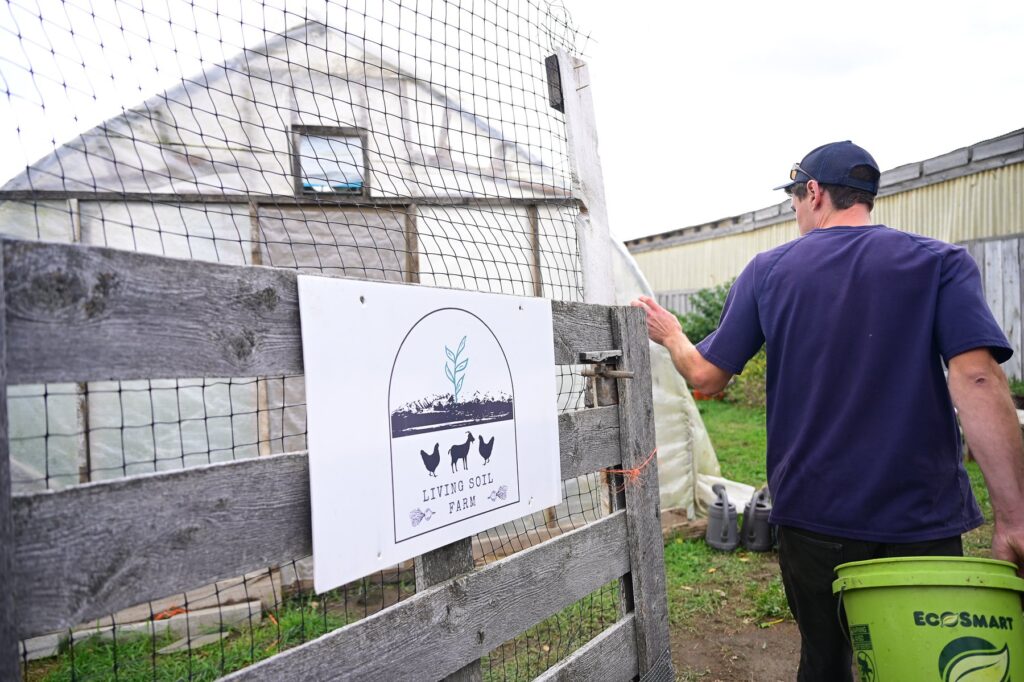man walking through a farm gate with LIVING SOIL FARM logo on the door