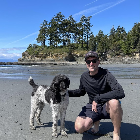 Man and dog on beach with trees and cliff