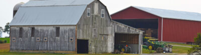 two barns at the edge of a field with tractors parked