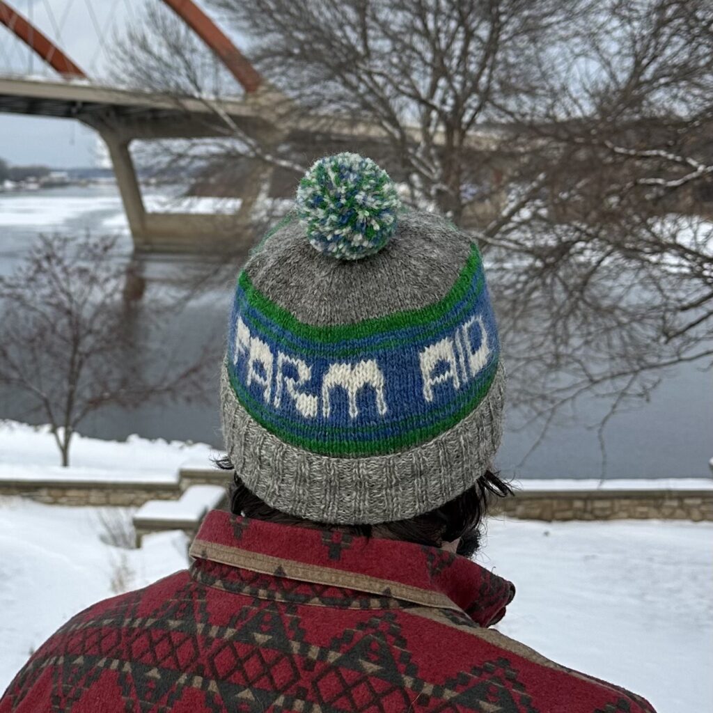 Person wearing a FARM AID wool hat in front of a bridge