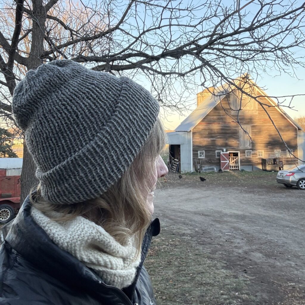 Person wearing a grey hat in front of a barn